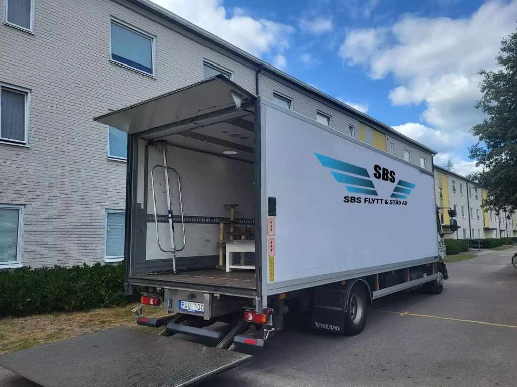 Flyttlastbil med öppet skåp och nedfälld lift för lastning.