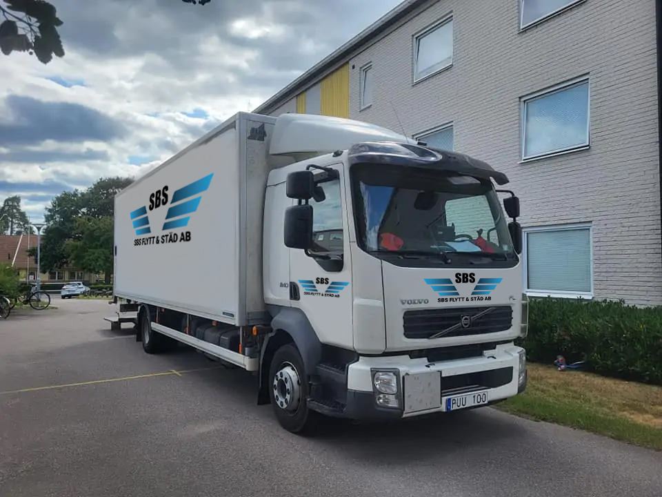 Flyttlastbil nära entrén till lägenhetshus för lättare flytthjälp.