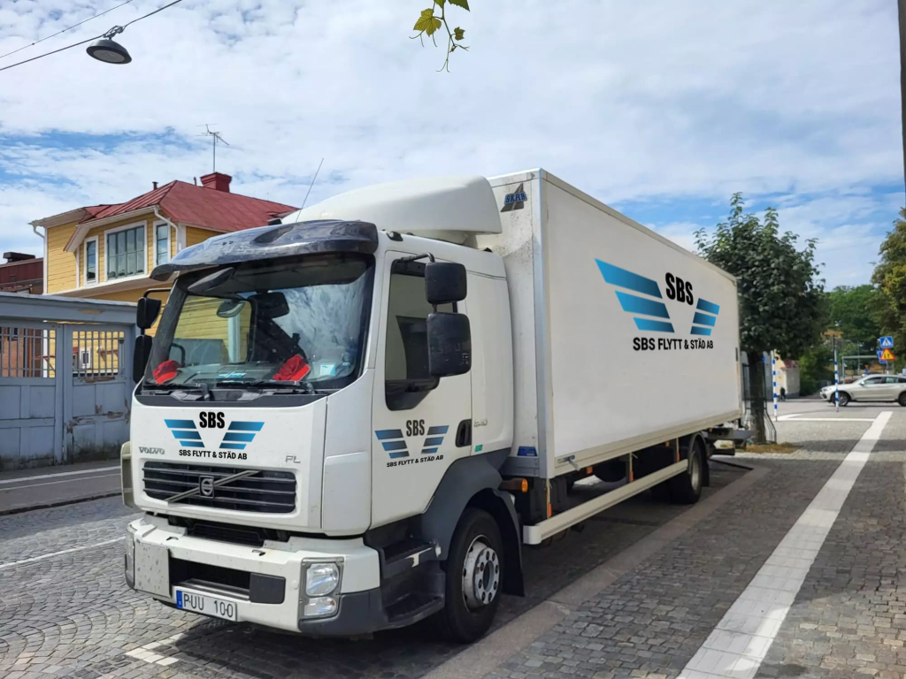 Flyttlastbil med nedfälld baklift i stadsmiljö under pågående lastarbete.